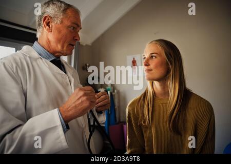 Männlich Arzt Durchführung von Blutdruckmessung an weiblichen Patienten, diskutieren Ergebnisse Stockfoto