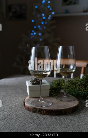 Party-Geschenkbox und Gläser Weißwein auf dem Tisch, mit defokussed Weihnachtsbaum Lichter. Weihnachten zu Hause Stockfoto