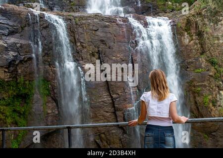 Ein Mädchen steht vor einem Wasserfall und bewundert Die schöne Aussicht Stockfoto