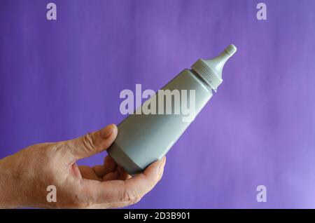 Männliche Hand und graue Plastikflasche mit Sirup. Der Mann hält eine neue Flasche Süßsirup für Eis und Desserts. Selektiver Fokus. Stockfoto
