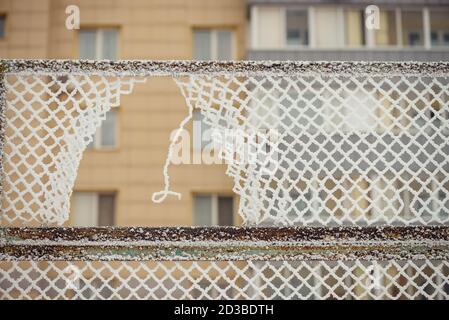 Ein Loch im Zaun. Rabitsa im Raureif. Ein mehrstöckiges Gebäude auf einem Hintergrund. Stockfoto