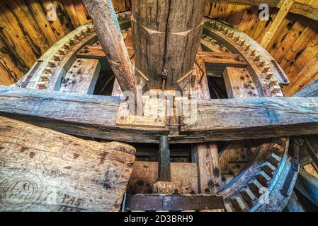 Holzkäfig mit einem Schaft, der zum Antrieb eines Schleifsteins in einer ländlichen Windmühle für Weizenmahlen verwendet wird. Industrieller Innenraum mit einem Zahnrad, das durch Klingen bewegt wird Stockfoto