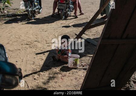 Ngwesaung, Myanmar - 26. Dezember 2019: Ein junges burmesisches Kind in einem bunten Kleid sitzt am 26. Dezember 2019 in Ngwesaung Myanmar im Sand und den Wellen Stockfoto