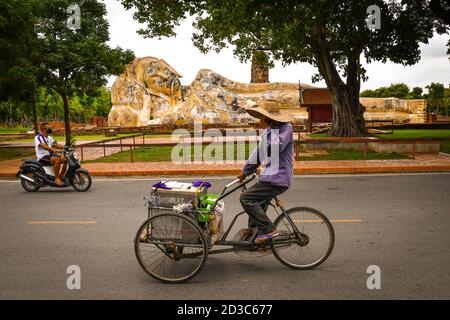 Ein Dreirad mit einem Korb, der vor einer liegenden buddha-Statue vorbeifährt. Dies ist ein typischer Transport in Asien. Stockfoto