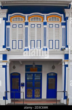 Restauriertes chinesisches Ladenhaus im peranakan-Stil mit weißen Wänden und kontrastierenden blau gestrichenen Fensterläden und Verzierungen. Stockfoto