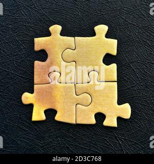 Vier gelbe Puzzleteile isoliert auf einem strukturierten schwarzen Hintergrund. Stockfoto