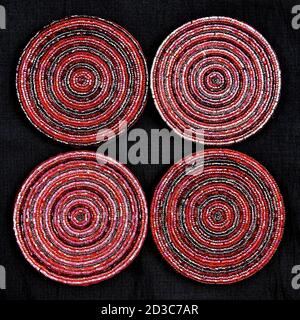 Eine Luftaufnahme eines Musters, das von vier roten und rosafarbenen runden Beaded Drinks Coasters auf schwarzem Hintergrund geschaffen wurde. Stockfoto