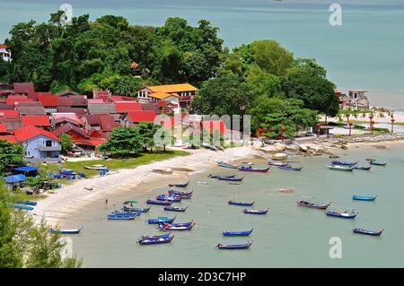 Ein Fischerdorf in Asien mit roten Ziegeldächern und bunten Fischerbooten, die in einem ruhigen Hafen festgemacht sind. Stockfoto