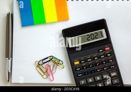 Taschenrechner mit Aufschrift '2021', weiße Note, farbiges Papier, Büroklammern, Stift. Geschäftskonzept, Kopierbereich. Stockfoto