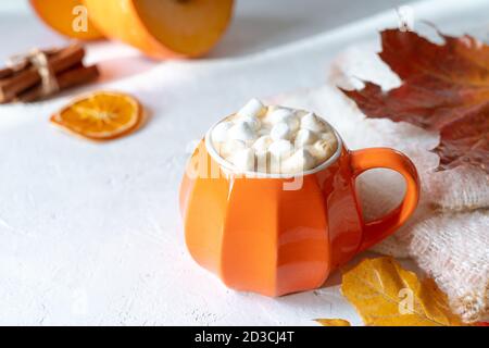 Komposition mit orangefarbenem Kürbis-Stil Tasse Kaffee mit Marshmallows und Herbstdeko, gefallenen Blättern, gemütlichem Pullover auf weißem Hintergrund. Stockfoto