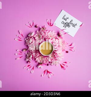 Stillleben Foto Draufsicht Karte mit Inschrift aber ersten Kaffee, Kaffee mit Milch in einer Tasse mit Chrysantheme Blumen um sie auf einem rosa Hintergrund. Stockfoto