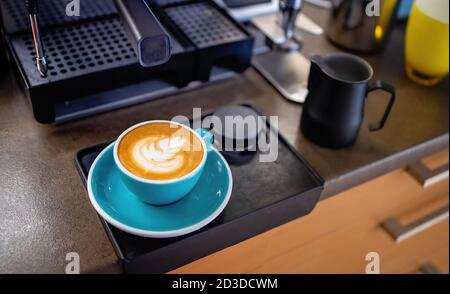 Latte Kaffee Zubereitung von Amateur zu Hause. Eine Tasse frischer Cappuccino, zubereitet zu Hause. Kaffeemaschine und Küche im Hintergrund. Home Barista Stockfoto