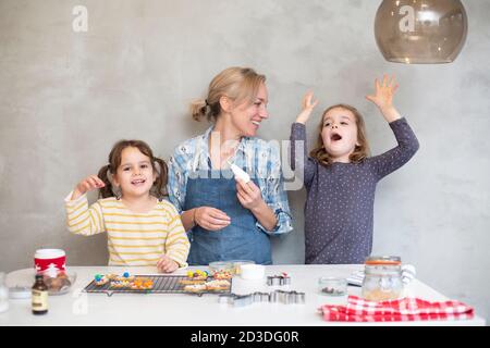 Blonde Frau trägt blaue Schürze und zwei Mädchen backen Weihnachtsplätzchen. Stockfoto