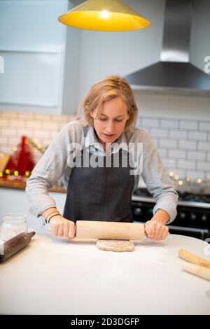 Blonde Frau trägt blaue Schürze stehen in der Küche, Backen Weihnachtsgebäck. Stockfoto