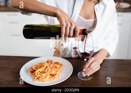 Beschnittene Ansicht einer Frau, die in der Nähe Rotwein in Glas gießt Teller mit Spaghetti Stockfoto