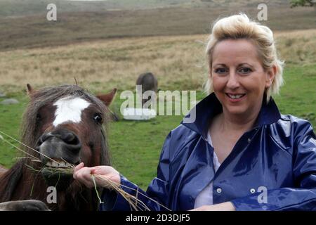 Weiß kaukasisch gefärbte blonde Frau mittleren Alters in ihren 40er Jahren trägt einen blauen glänzenden PVC-Regenmantel aus einem Second-Hand-Shop gekauft. Kuscheln und streicheln Ponys und Pferde Stockfoto