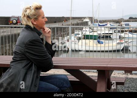 Weiß kaukasisch gefärbte blonde Frau mittleren Alters in ihren 40er Jahren trägt eine Lederjacke aus einem Second-Hand-Shop gekauft. Sie läuft um den Hafen herum und sieht nachdenklich aus Stockfoto