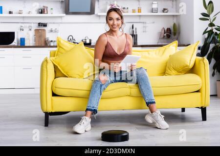 Frau, die in der Nähe des Roboter-Staubsaugers sitzt und die Kamera anschaut Stockfoto