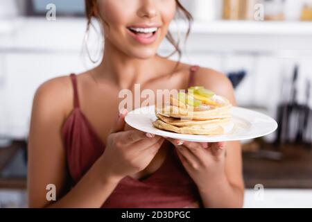 Beschnittene Ansicht der jungen Frau, die Pfannkuchen mit frischem Obst hält In der Küche Stockfoto