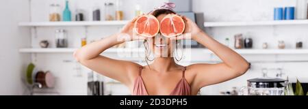 Panoramaaufnahme einer jungen Frau, die eine Hälfte der Grapefruit in sich hält Küche Stockfoto