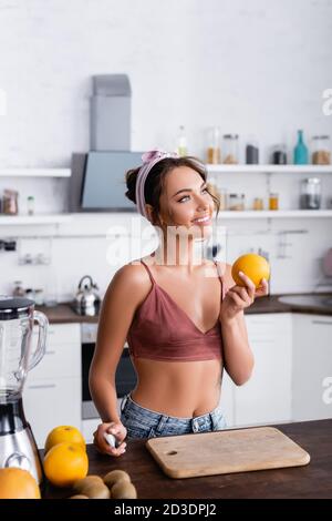 Selektiver Fokus der Hausfrau hält Orange und Messer in der Nähe des Schneidens Brett und Mixer Stockfoto