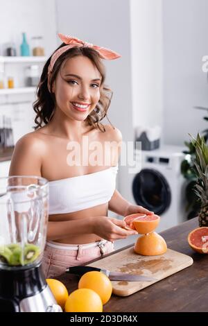 Selektiver Fokus der Hausfrau hält die Hälfte der Grapefruit in der Nähe von Früchten Und Mixer zu Hause Stockfoto