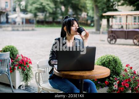 Arbeiten online, freiberufliches Konzept. Junge ziemlich intelligente asiatische Frau genießen die Kaffeepause, mit Laptop-Computer, sitzen am Tisch in der Stadt Café Stockfoto