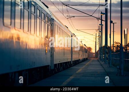 Eisenbahn bei Sonnenaufgang. Personenzug von Bahnhof entfernt. Stockfoto