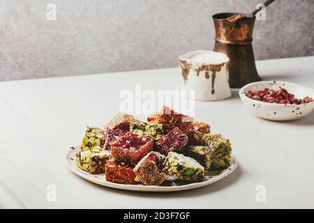 Auswahl an traditionellen türkischen Dessert Turkish Delight unterschiedlichen Geschmack und Farben Rosenblätter und Pistazien auf Keramikteller mit Kaffee jezve ein Stockfoto
