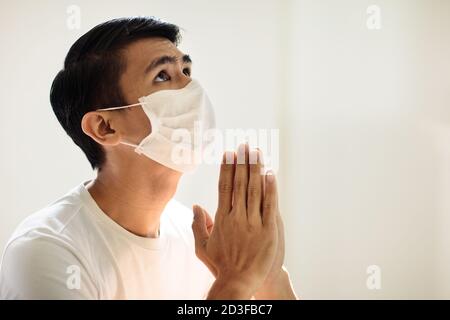 Betet für das Opfer des Coronavirus. Asiatischer Mann im Gesicht Maske beten für krank. Patient in Krankenhauskapelle oder Kirche während Covid-19 Ausbruch. Viruspandemie. P Stockfoto