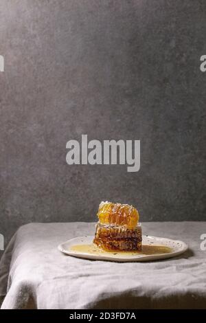Bio Honig in den Waben in beschmutzt Keramikplatte auf Leinen Tischdecke mit grauen Wand im Hintergrund. Stockfoto