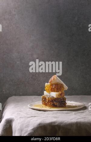 Bio Honig in den Waben mit Scheiben Brot aus Weizen in beschmutzt Keramikplatte auf Leinen Tischdecke mit grauen Wand im Hintergrund. Stockfoto