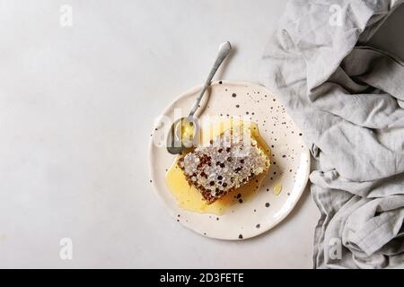 Bio Honig in den Waben mit Löffel in beschmutzt Keramikplatte auf Leinen über weißem Marmor Hintergrund. Flach, Kopie, Raum Stockfoto