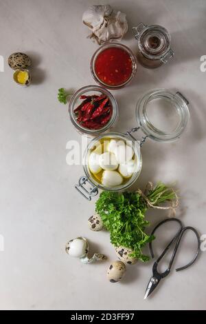 Zutaten für selbstgemachte mariniert marinierte Wachteleier. Gekochte Eier in Olivenöl, Tomatenmark, Paprika in Töpfen, frische Petersilie, Schere über whi Stockfoto