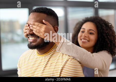 Glückliche afroamerikanische Frau, die die Augen des Mannes schließt Stockfoto