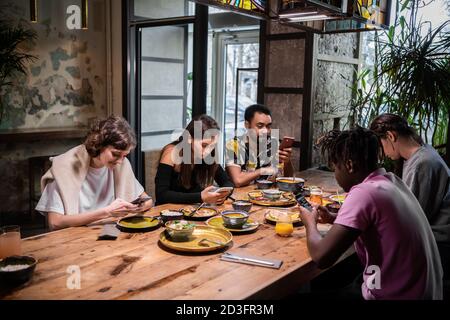 Eine multikulturelle Gruppe von Studenten, die eine Mahlzeit in einem Café teilen und kostenloses WLAN nutzen. Stockfoto