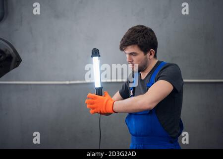 Ein Mann in Overalls und Arbeitshandschuhen hält eine Taschenlampe Stockfoto