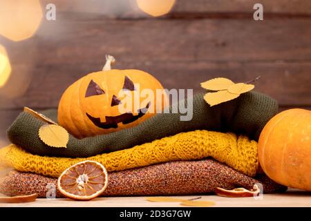 Halloween Kürbis und Stapel von bunten Winter Pullover auf Holz. Gemütliche Herbstdekoration mit Laterne Stockfoto