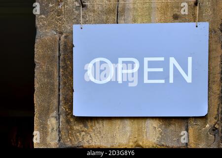Nahaufnahme des blauen länglichen Metalls offenes Schild mit Weiß Text außen hängend mit Schnur an Steinwand Stockfoto