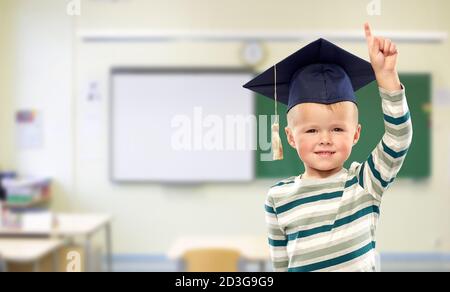 Junge im Mörserbrett zeigt Finger nach oben in der Schule Stockfoto