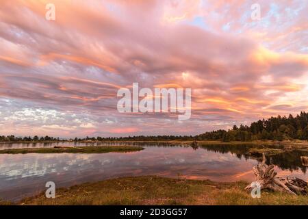 Wenn man in die Ferne blickt, spiegeln sich die Sonnenuntergänge über der Mündung und die Wolken auf dem Wasser in Parksville, British Columbia. Stockfoto