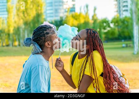 Ein glückliches schwarzes Paar, das bunte Zuckerwatte zusammen in einem Park einer großen Stadt hat. Stockfoto