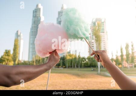 Ein glückliches schwarzes Paar, das bunte Zuckerwatte zusammen in einem Park einer großen Stadt hat. Stockfoto