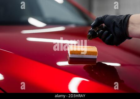 Auto Detaillierung - Mann trägt Nano-Schutzbeschichtung oder Wachs auf roten Auto. Abdeckung der Motorhaube mit einer Flüssigglaspolitur. Stockfoto