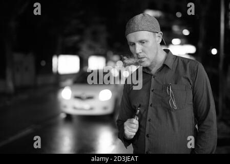 Reifer Mann rauchen Elektronische Zigarette in den Straßen bei Nacht Stockfoto