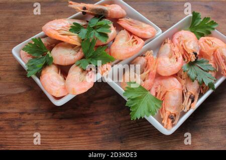 Gekochte rosa Garnelen in der Schale mit Petersilie serviert. Muschelgarnelen auf den weißen Tellern auf dem rustikalen Holztisch. Draufsicht, Kopierbereich Stockfoto