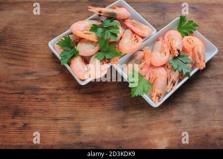 Gekochte rosa Garnelen in der Schale mit Petersilie serviert. Muschelgarnelen auf den weißen Tellern auf dem rustikalen Holztisch. Draufsicht, Kopierbereich Stockfoto