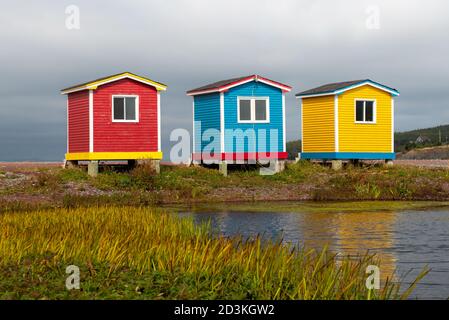 Drei bunte und helle Schuppen am Meer mit Herbstlaub im Vordergrund. Die Gebäude sind rot, blau und gelb. Stockfoto