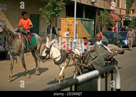 Blick auf die Straße in Kairo. Ein Mann in einem Eselkarren mit einem Jungen. Ein anderer Junge reitet ein Pferd nebenan Stockfoto