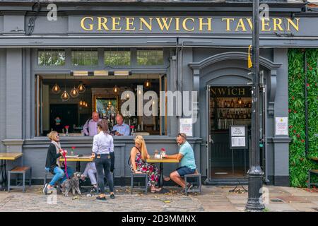 Auf dem Bürgersteig vor der Greenwich Tavern in der Nähe des Royal Maritime Museum in Greenwich, Lo, genießen die Menschen einen "gesellschaftlich distanzierten" Drink in der Sonne Stockfoto